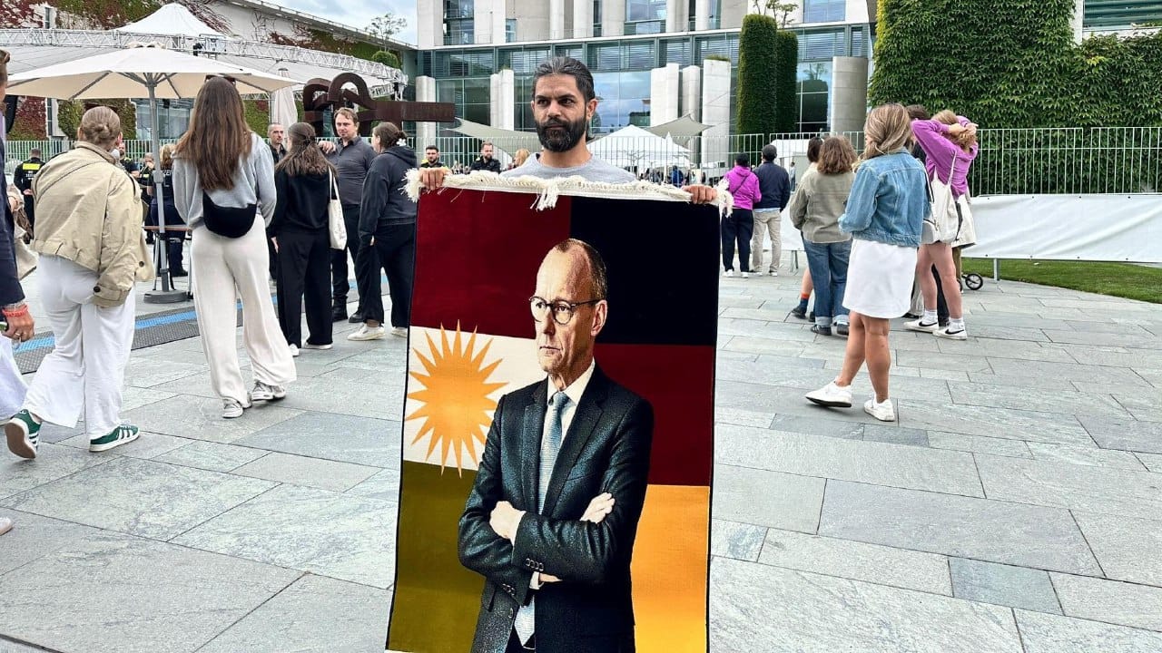 کوردێک وێنەی ڕاوێژکاری ئەڵمانیا بە ئاڵای کوردستان و ئەڵمانیا دەنەخشێنێت